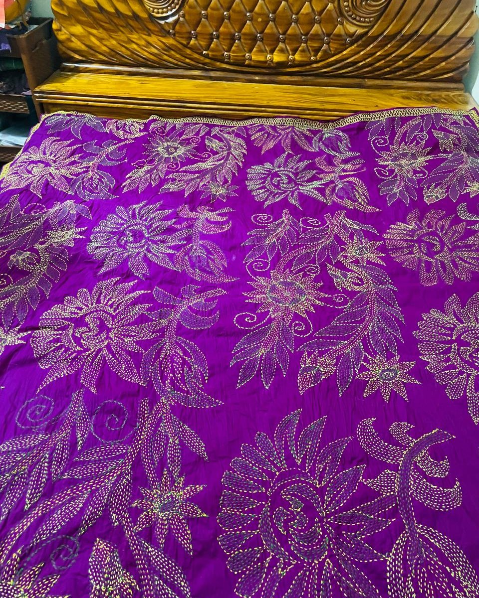 Purple nakshi kantha bedspread spread across a carved wooden bed